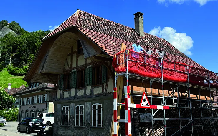Eingerüstetes Berner Bauernhaus mit Ziegeldach, drei Mitarbeiter von Sterchi Bedachungen auf dem Gerüst