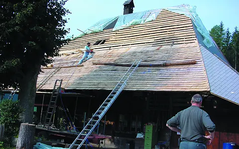 Bauernhaus mit teilweise abgedecktem Dach, provisorisch mit einer Blache geschützt, ein Dachdecker arbeitet auf der Fläche